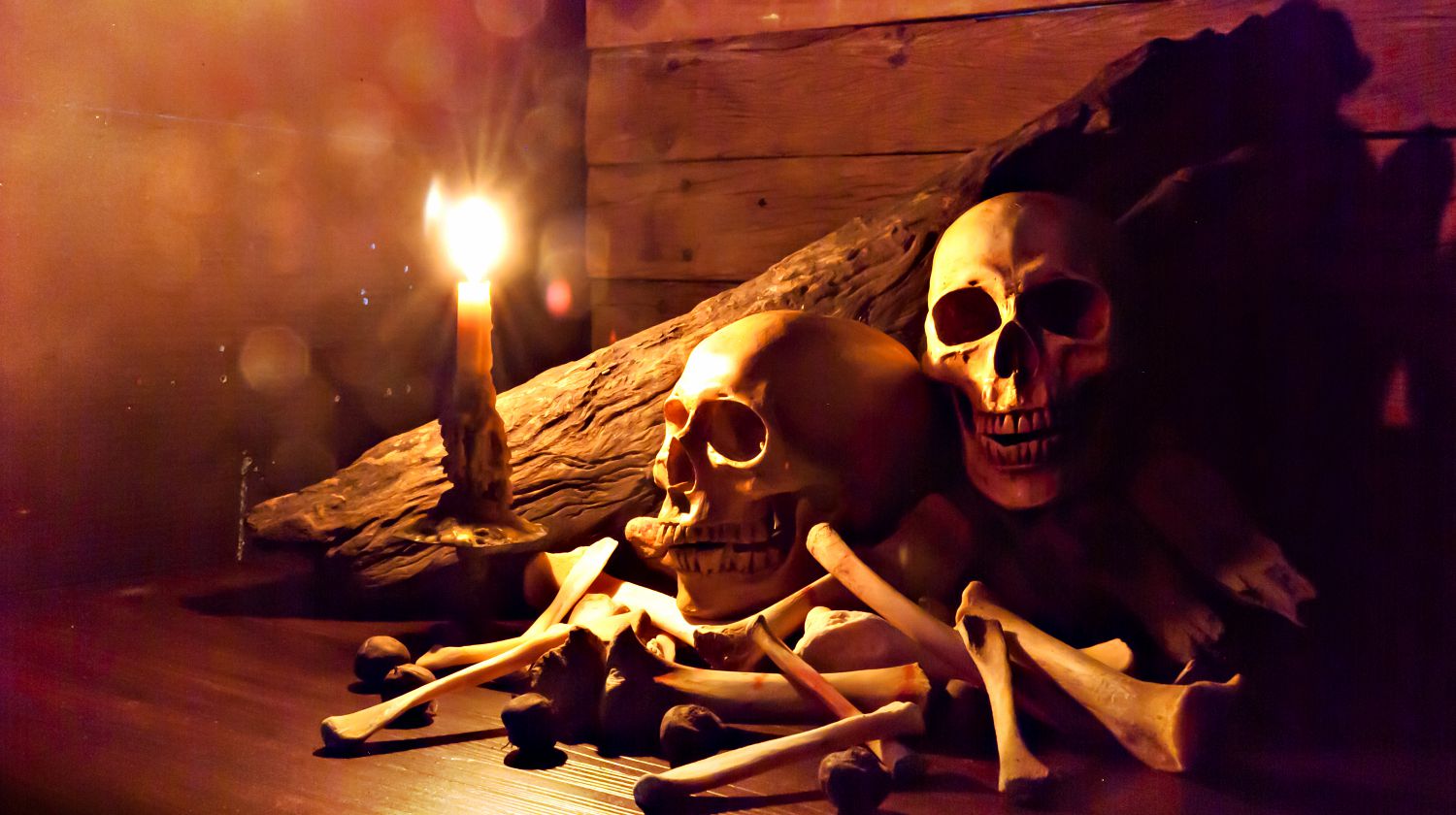 Candle lighting of skulls and bones pile with candle on wooden floor and old dirty wall | DIY Halloween Skull And Bones For Decorations | Featured