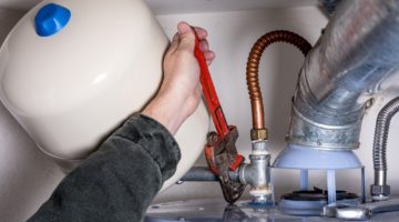 man-works-on-hot-water-heater | 18 Helpful Tips for Water Heater Tune Up To Save Up This Winter | Featured