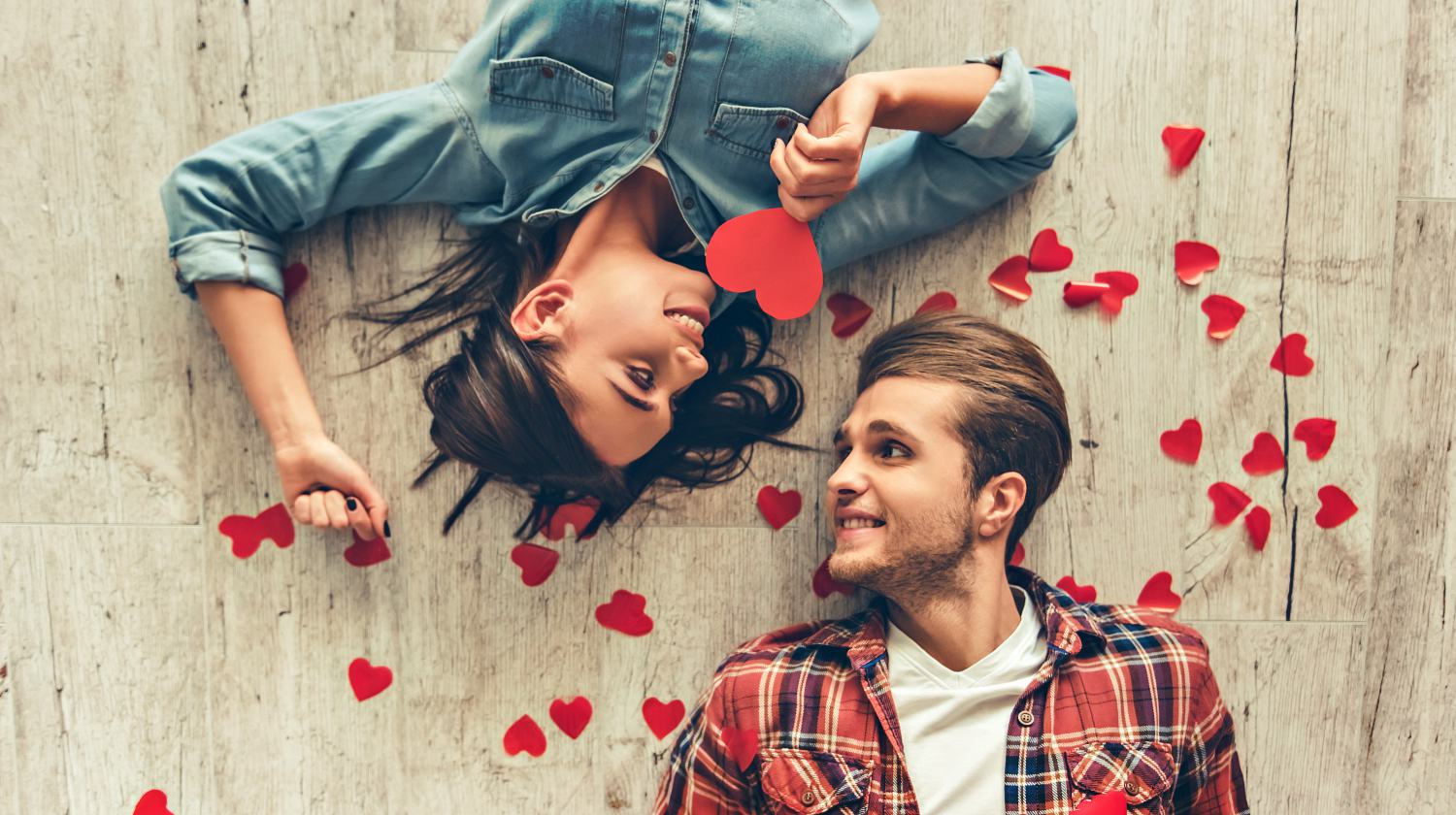 Feature | Smiling couple looking at each other while lying on wooden floor | Valentine's Day Ideas for Him and Her