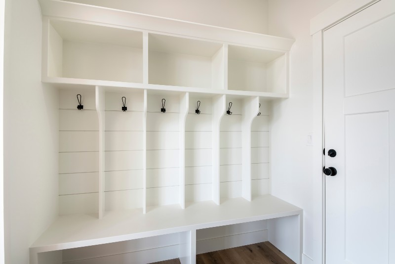 Interior of a white mudroom with white garage door and wooden flooring | Mudroom In The Garage Entry