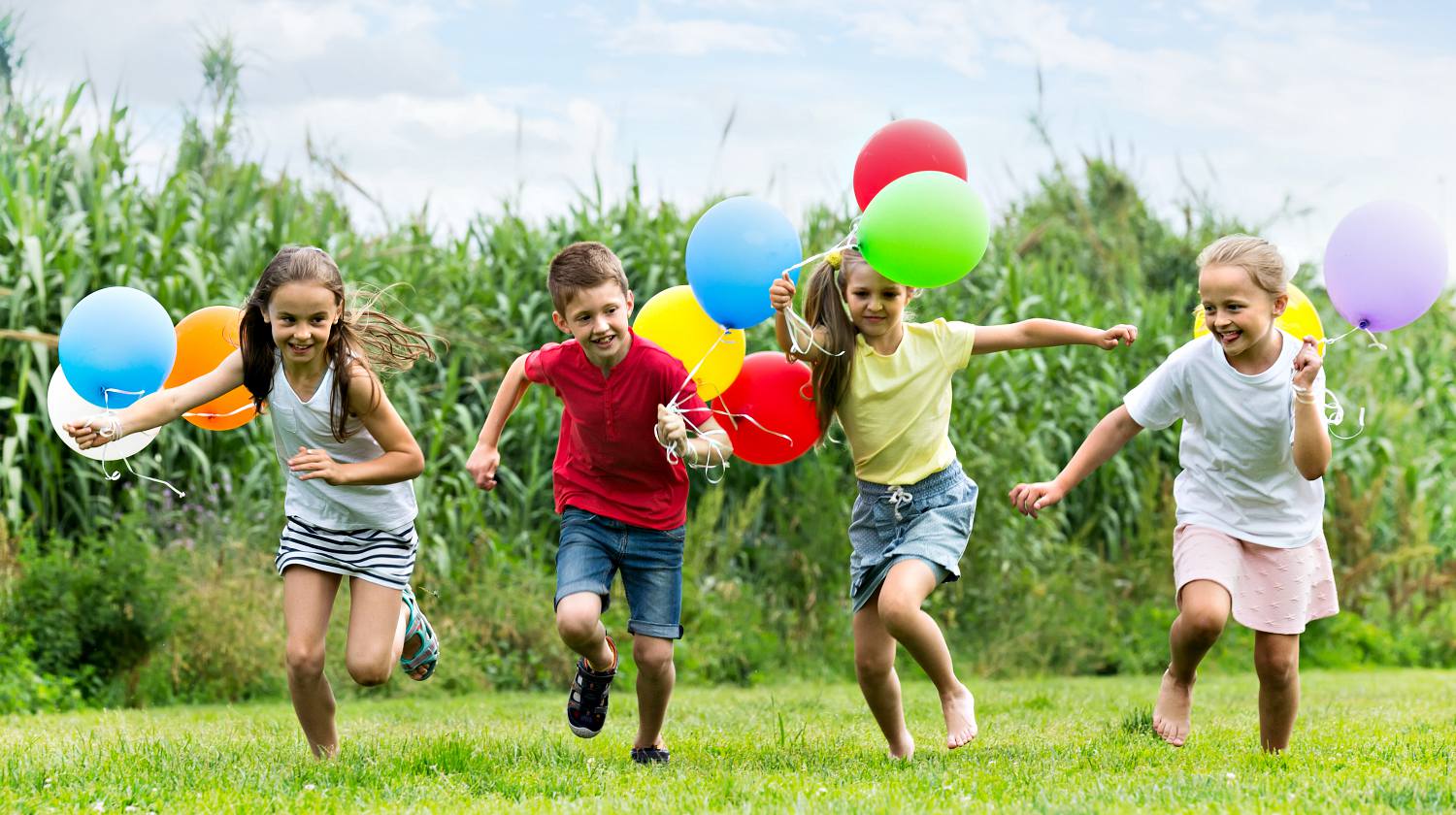 Feature | Cheerful smiling boy and girls holding air balloons and running in summer park | DIY Summer Games To Entertain Kids This Weekend