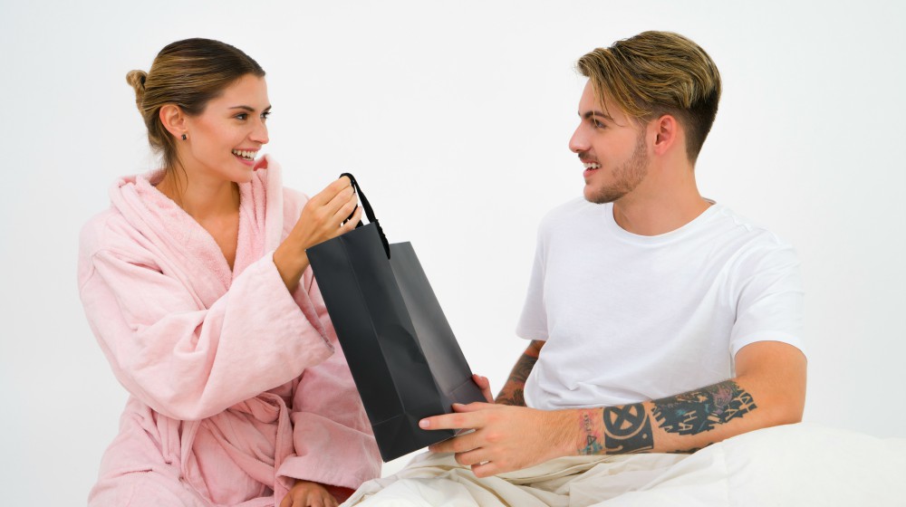woman surprising boyfriend with a gift | Amazing Manly Christmas Gift Ideas For Boyfriend | Manly Christmas Gift Ideas | masculine gifts | Featured