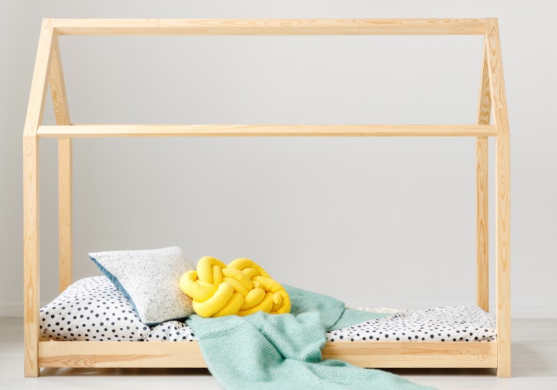 Child toys on shelves on a white wall and a wooden house bed frame for a toddler | Two Toddler Beds For $75
