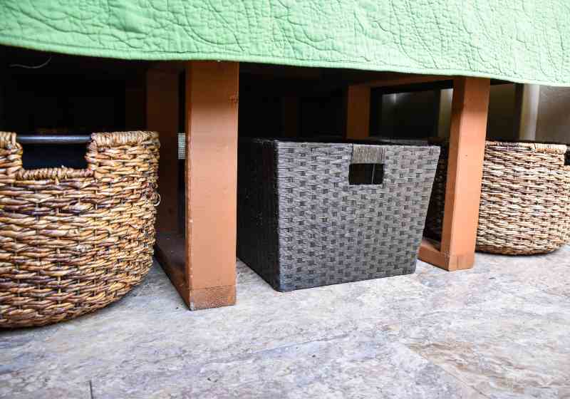 three wicker baskets in a row under a bed with green blanket overhang organization | DIY Platform Bed With Storage And Baskets