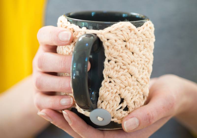 Hands holding a mug in knitted cozy | Marion’s Cozy Mug Warmer