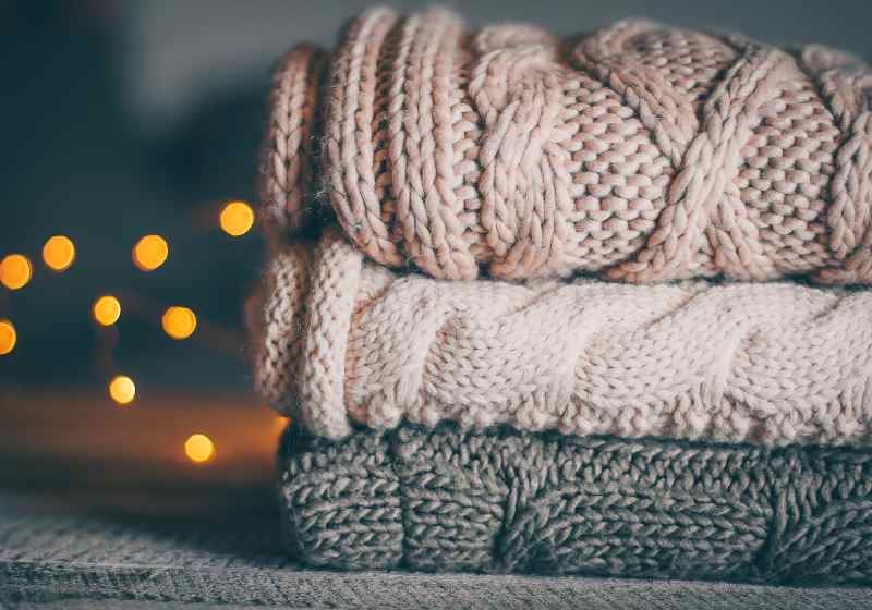 Stack of cozy knitted sweaters and garland lights | Soft Blanket | Ultimate Beginners Crochet Pattern