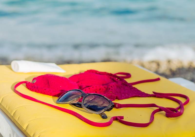 Sun glasses, sun screen lotion and crochet bra on a yellow mattress on a beach | Unique Crochet Bathing Suit