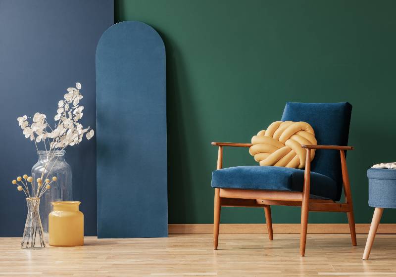 Yellow pillow on wooden armchair in blue and green flat interior with flowers and stool | Knot Pillow