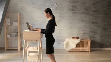 Asian woman typing on laptop at stand-up workplace | Build Your Own DIY Standing Desk For Your Home Office | Featured