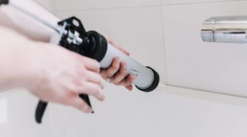 hands-man-putting-silicon-tube-bathroom | How to Recaulk a Bathtub | Featured