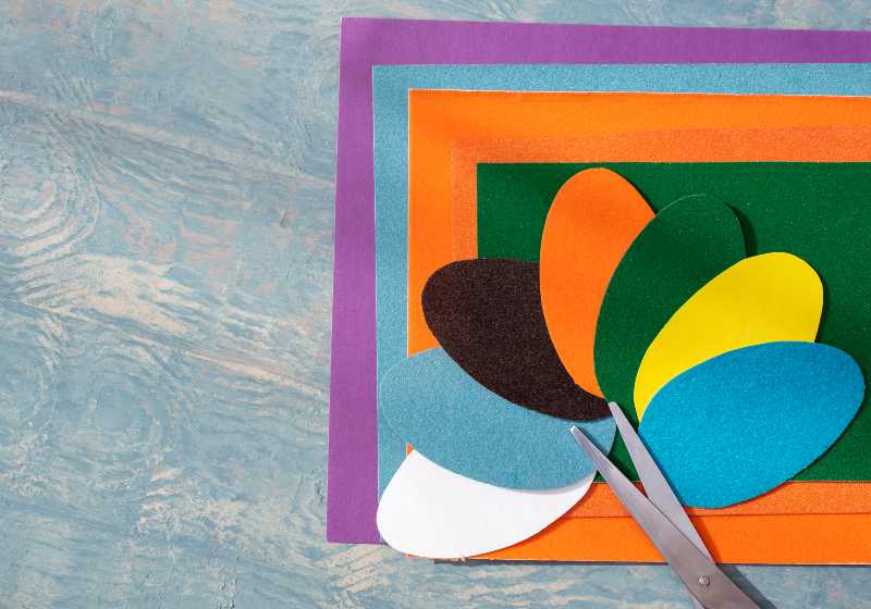 Cut out colored Easter paper eggs, pattern and scissors on colorful paper on a blue wooden table | Apply Monotone Color Scheme