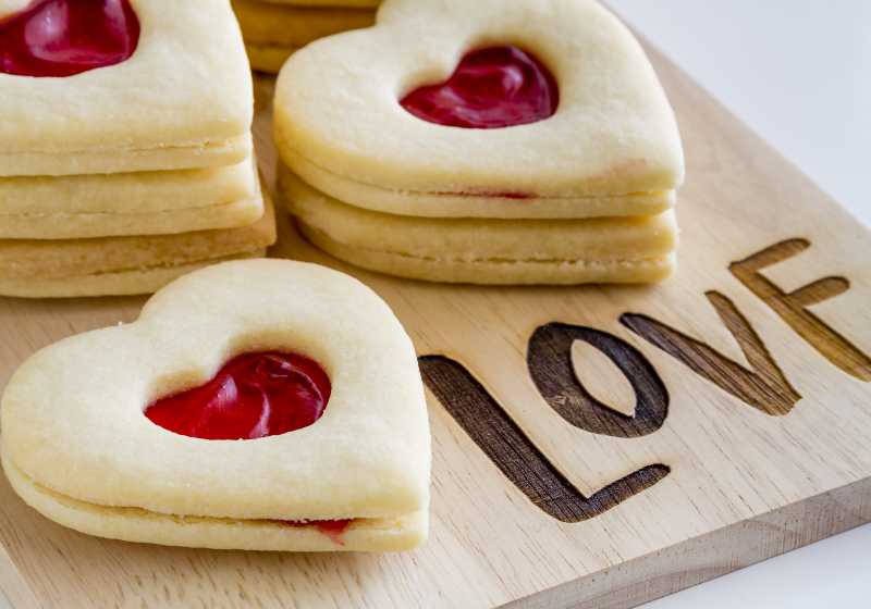 Heart shaped linzer cookies filled with strawberry jam sitting on wooden cutting board with word love etched in wood | Etched Cutting Boards