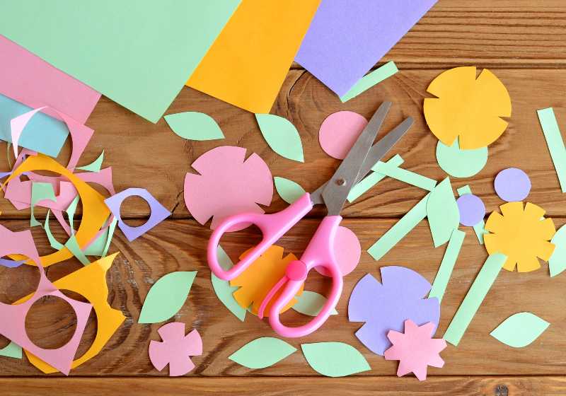 Paper flowers, paper sheets, scissors, paper scrap on a wooden table | Scrapbook with Plenty of Colors