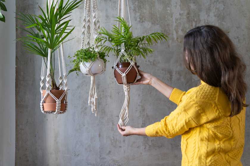 Woman gardener holding macrame plant hanger with houseplant over grey wall | DIY Hanging Planter