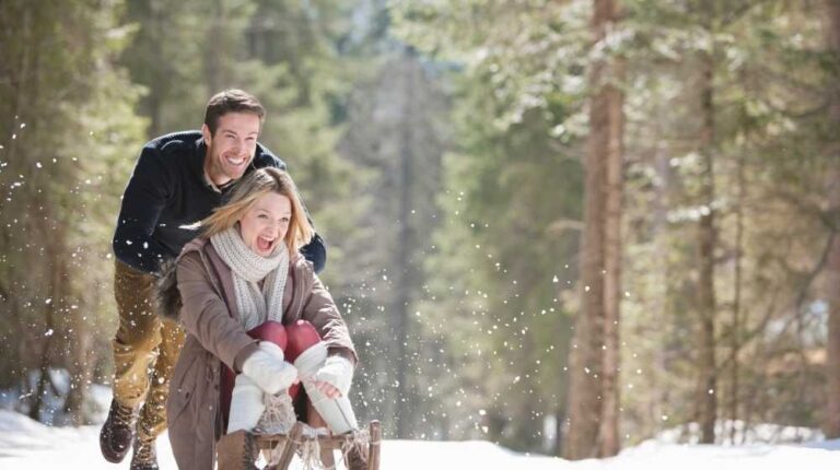 man-pushing-woman-on-sled-in-snowy-woods | How To Make A Wooden Sled Your Kids Can Enjoy This Winter | Featured