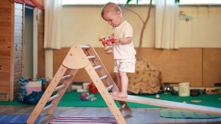 child-standing-on-pikler-triangle-red | How To Make A DIY Pickler Triangle For Your Child's Independent Play | Featured