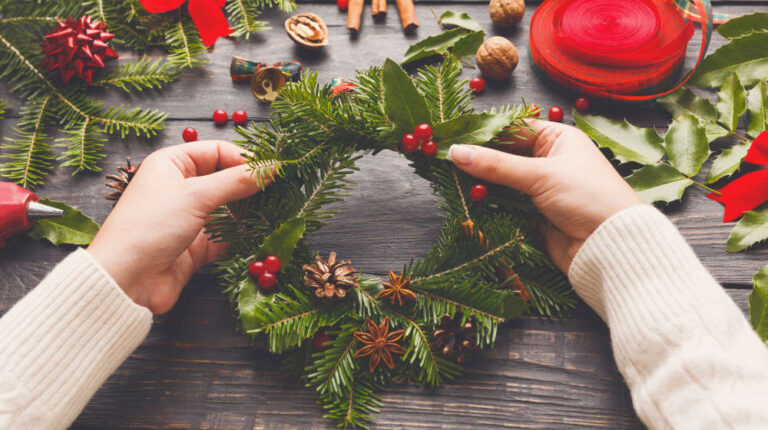Wooden table with female hands making christmas wreath | DIY Christmas Wreaths You Will Love | handmade christmas wreaths | Featured