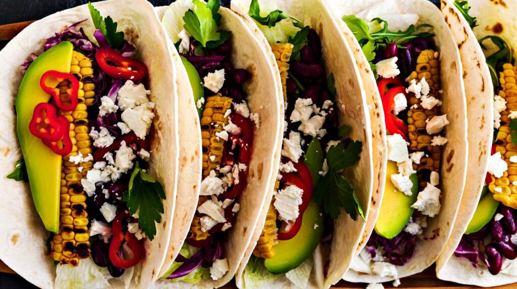 Feature | Mexican tacos with avocado, grilled corn, red cabbage slaw and chili salsa on wooden board black shale table | Cinco De Mayo Recipes To Get the Party Started