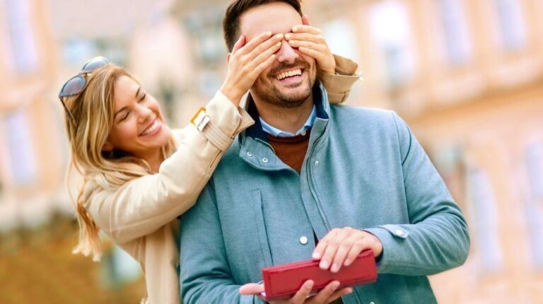 Young woman with giftbox closing his boyfriend eyes to make a surprise for him | DIY Anniversary Gifts For Him | Featured