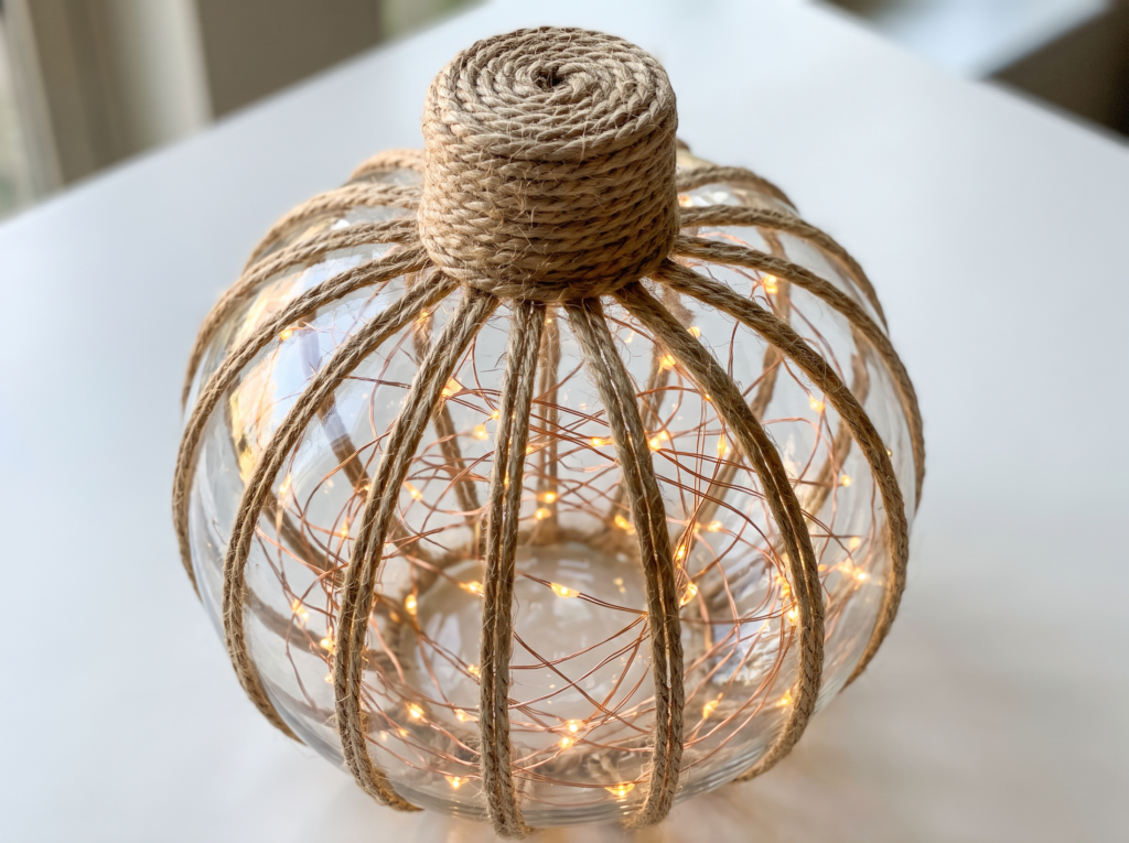 Short coiled jute twine stem glued onto the top of a glowing glass pumpkin wrapped in vertical twine ribs