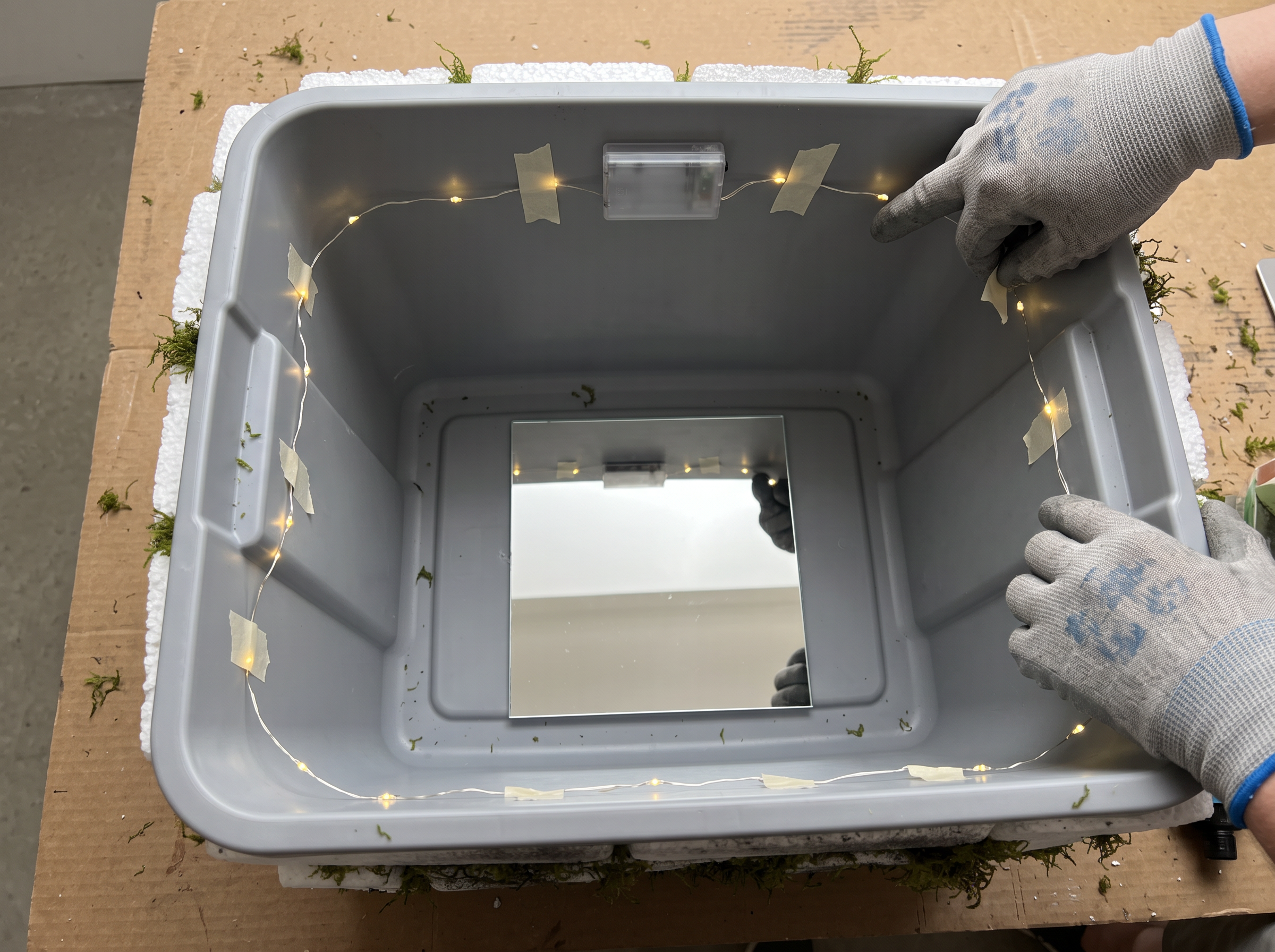 Mirror tile on the bottom of the bin with battery fairy lights taped in a ring around the inside wall and the battery box taped near the top