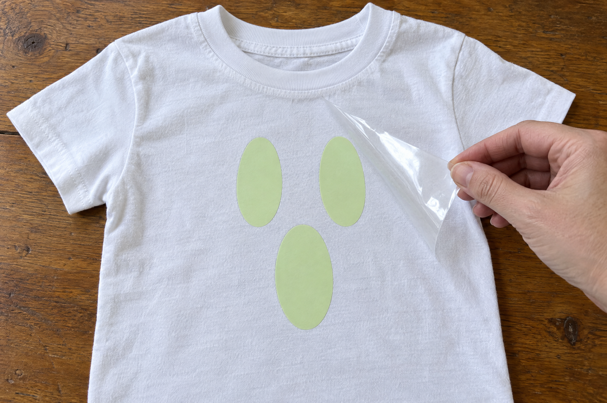 Peeling the carrier sheet off a glow-in-the-dark iron-on ghost face on a white tee