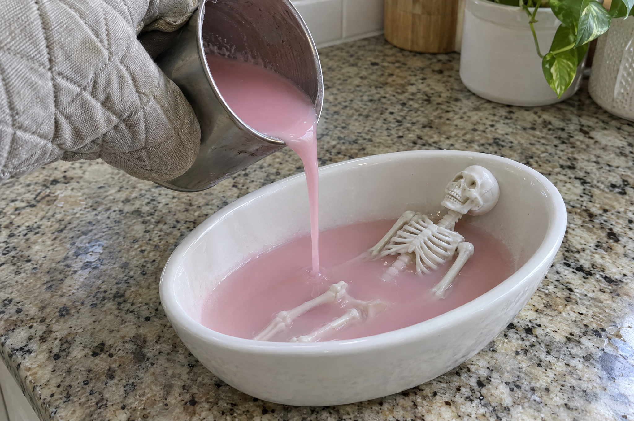 Pouring cooled pink wax around a mini skeleton in a ceramic bowl