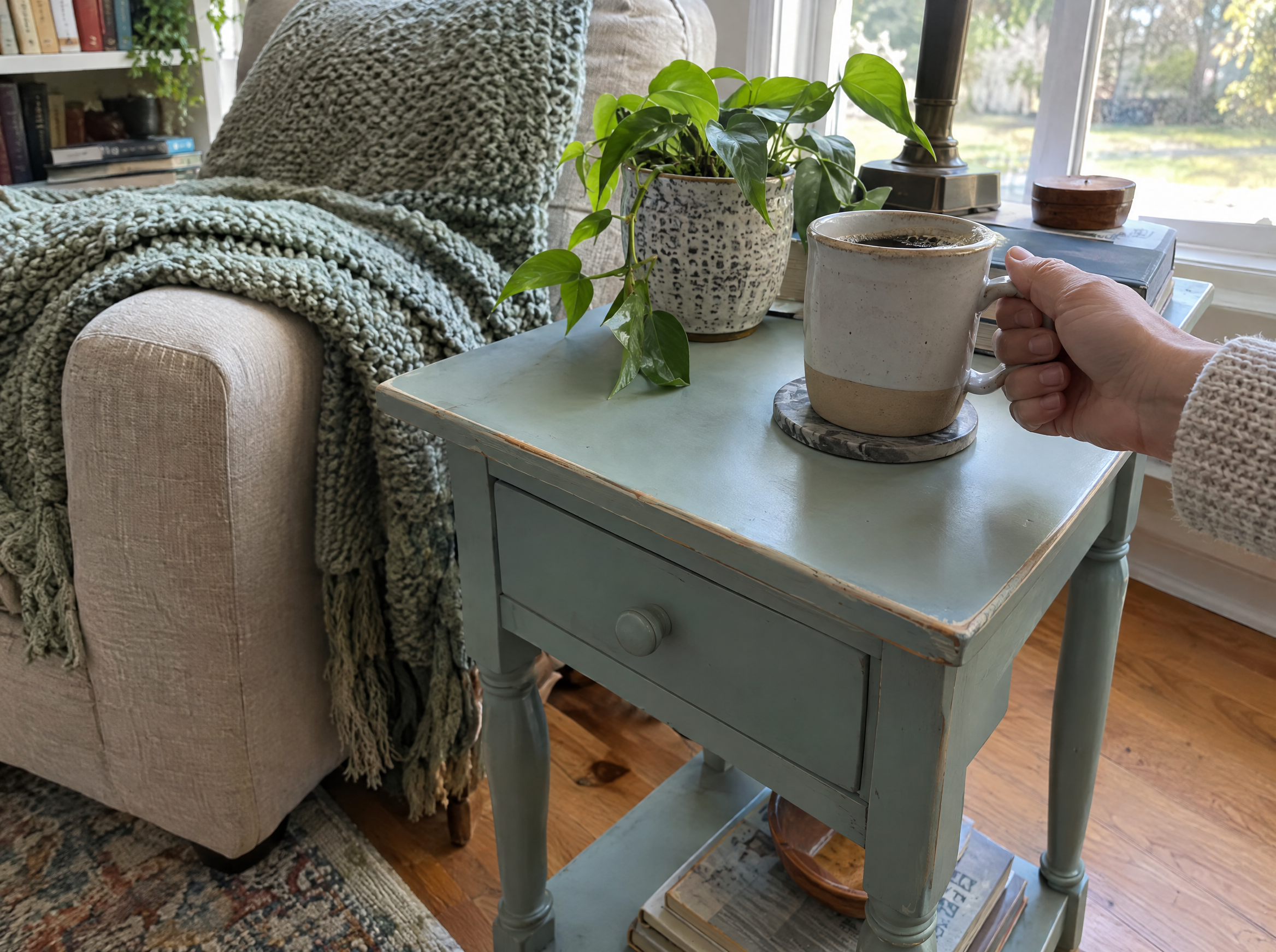 Soft blue chalk painted end table beside a reading chair with a knit throw