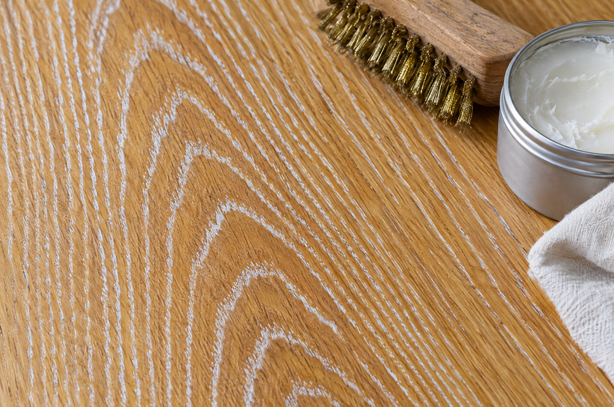 White liming wax filling the open grain of an oak tabletop, with a brass wire brush